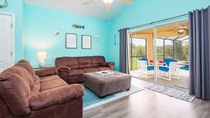 A living room with a brown leather sofa, a matching ottoman, and a glass door leading to an outdoor seating area. - Luxury 5 bed 4 bath SW facing pool with conservation and lake view (Clermont)