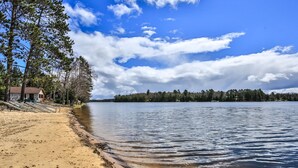 A beach with a sandy shore, a small wooden structure, and a forested shoreline.