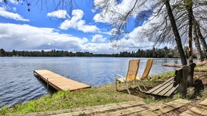 A wooden dock extending into a calm lake, with two wooden chairs facing the water.