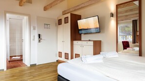 Habitación de hotel con techo de madera, cama con ropa blanca, televisor montado en la pared y ventana con vistas al exterior.