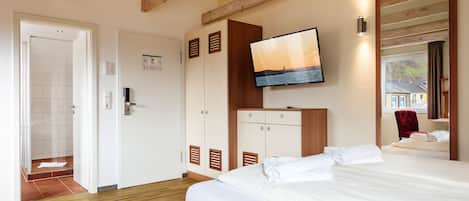 A hotel room with a wooden ceiling, a bed with white linens, a TV mounted on the wall, and a window with a view of the outside.