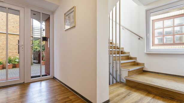 Un interior moderno con una escalera de madera, una puerta corredera de vidrio que da a un espacio exterior y un certificado enmarcado en la pared.