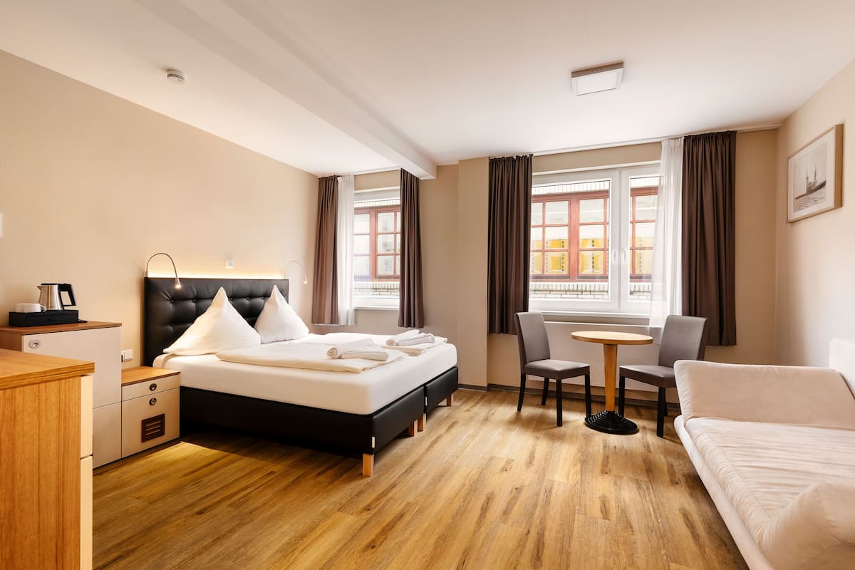Quarto de hotel com cama, mesa de cabeceira, cadeira e uma pequena mesa redonda.