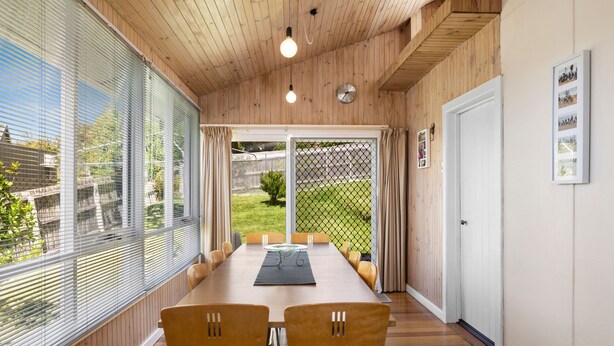 Uma sala de jantar com uma mesa comprida, duas cadeiras e vista para um quintal através de uma porta de vidro.