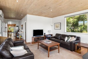 Ein modernes Wohnzimmer mit Holzboden, einem großen Fenster, einem Flachbildfernseher, einer Ledersofa, einem Couchtisch und einem Bücherregal.