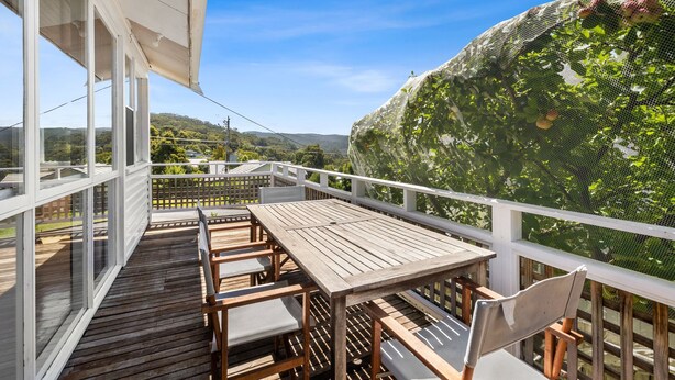 A wooden deck with a table and chairs, overlooking a lush garden with a mesh fence.