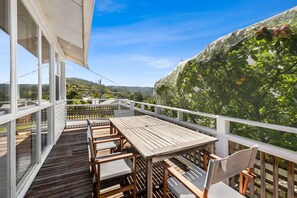Eine Holzterrasse mit Tisch und Stühlen, mit Blick auf einen üppigen Garten mit einem Maschendrahtzaun.