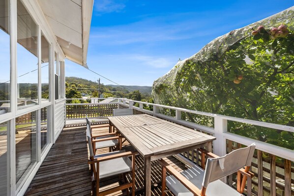 A wooden deck with a table and chairs, overlooking a lush garden with a mesh fence.