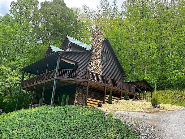 Uma cabana de toras com chaminé de pedra, varanda e alpendre.