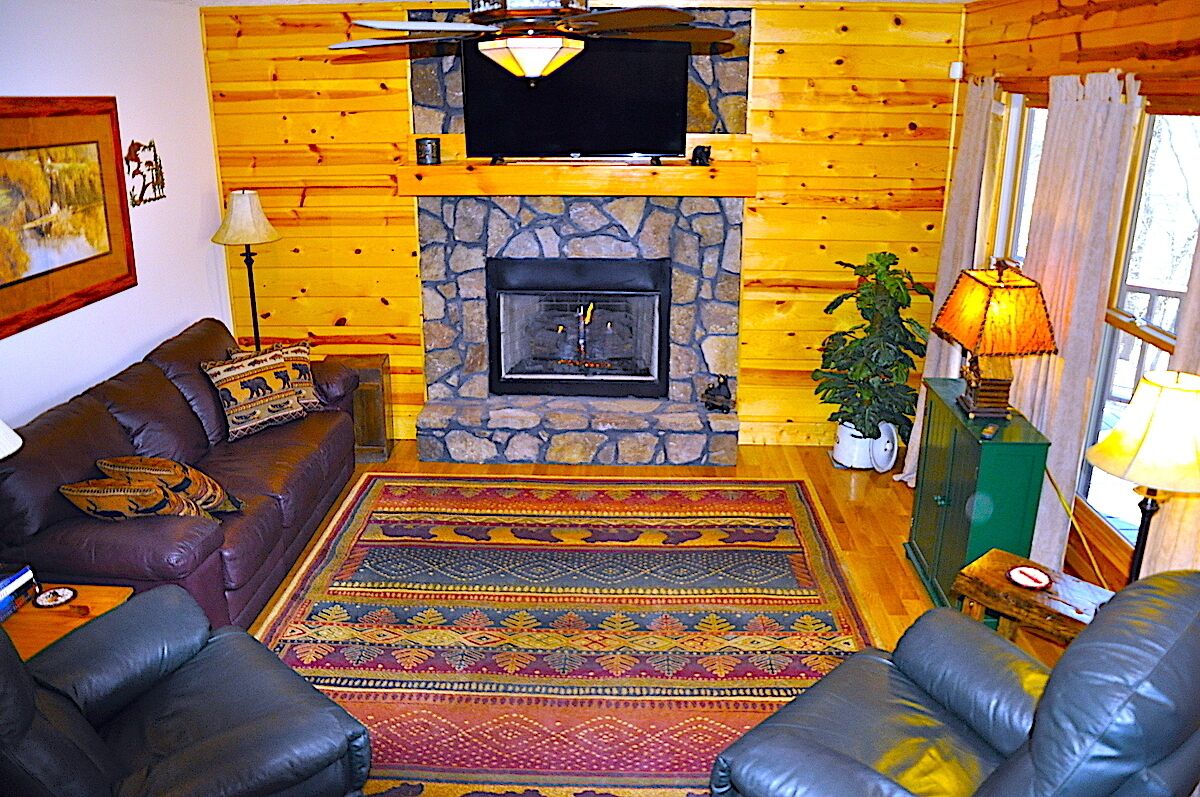 A cozy living room with a stone fireplace, leather sofas, and a colorful rug.