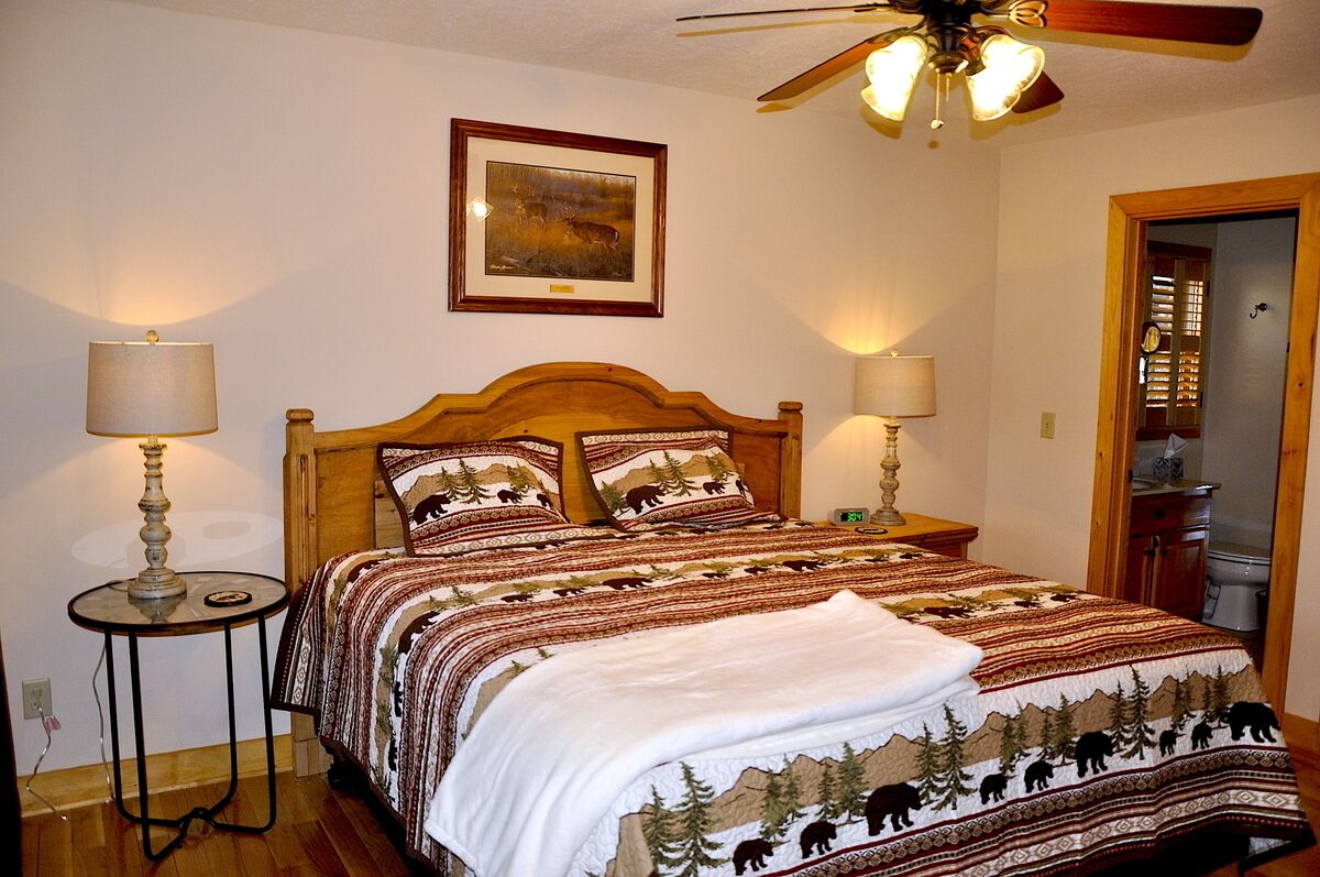 A bedroom with a wooden headboard, two bedside lamps, a framed picture on the wall, and a ceiling fan.