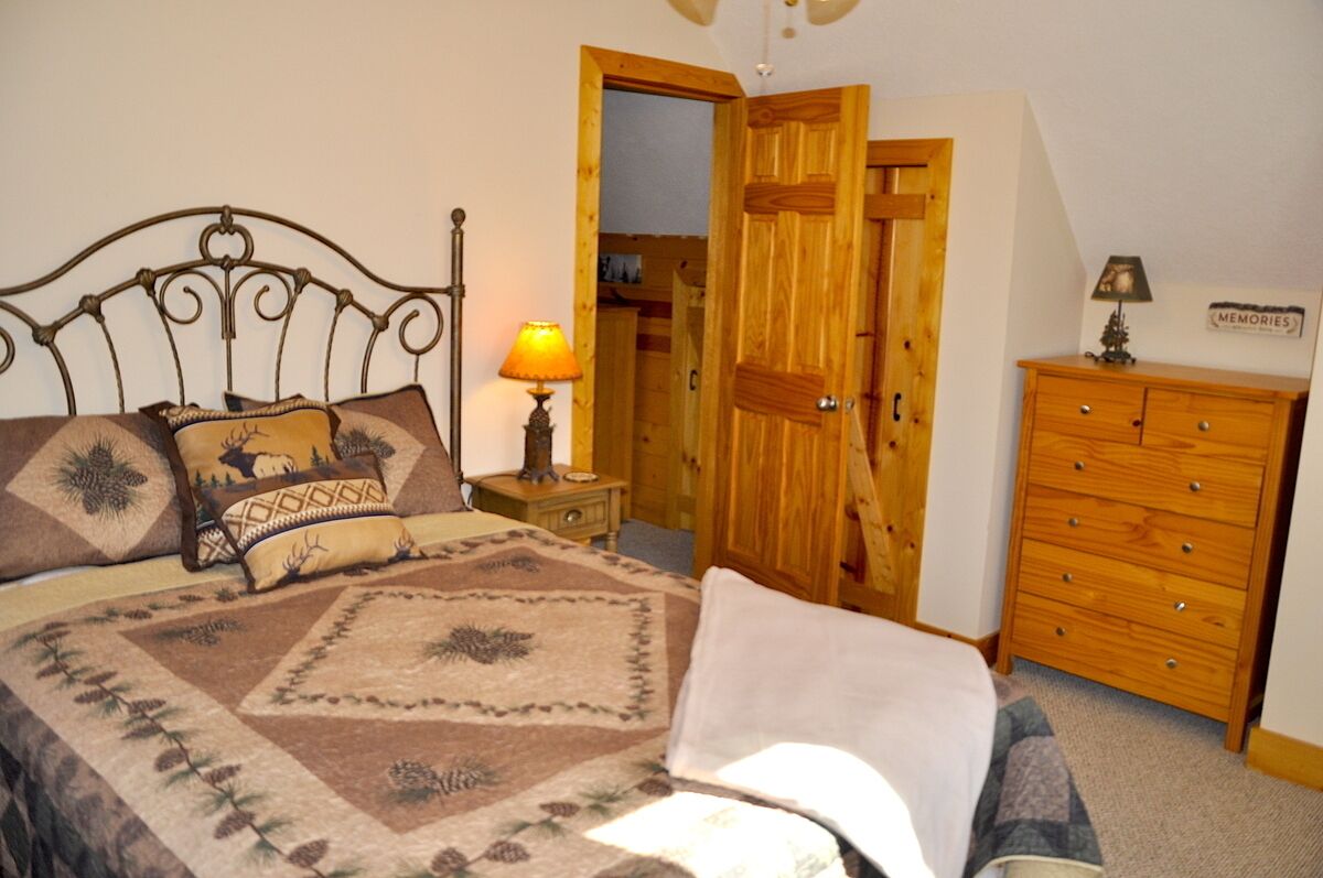 Une chambre à coucher comprenant un lit, une armoire en bois, une table de chevet avec une lampe, et une porte donnant sur une autre pièce.