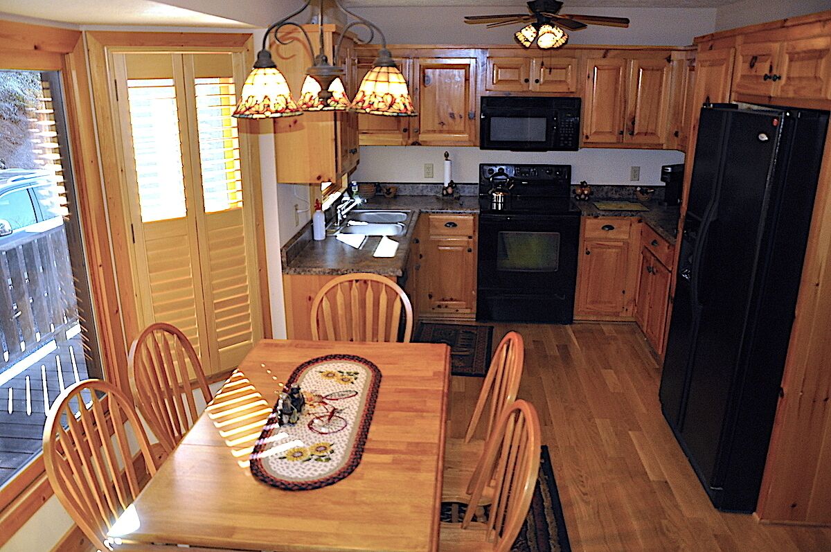 Une cuisine avec des meubles de rangement en bois, un réfrigérateur noir, un four à micro-ondes, un four traditionnel et une table à manger avec des chaises.