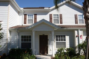 A two-story house with a central entrance, a brown door, and a small porch area with plants. - Lucaya Village Resort - 3 Beds and 2 Baths. ID: 57417 (Kissimmee)