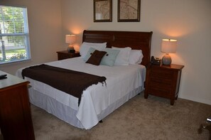 A neatly made bed with white bedding and a brown throw blanket, flanked by two bedside tables with lamps, in a room with a carpeted floor and a window with blinds. - Lucaya Village Resort - 3 Beds and 2 Baths. ID: 57417 (Kissimmee)