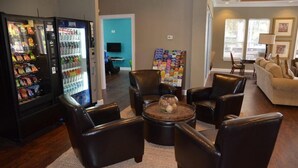 A lobby with a seating area featuring leather chairs and a coffee table, a vending machine, and a bulletin board.