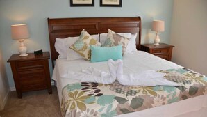 A neatly made bed with floral bedding, two bedside lamps, and a wooden nightstand with a drawer. - Lucaya 4 Bedrooms 3 Baths Townhome With Central Kitchen (Kissimmee)