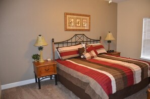 A bedroom with a bed, two bedside tables, a lamp on each table, a wall-mounted picture, and a window with blinds. - Lucaya 3 Bedroom 2 Bath First Floor Townhome (Kissimmee)