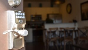Puerta con teclado numérico y cerradura, que da paso a una habitación con comedor y cocina.