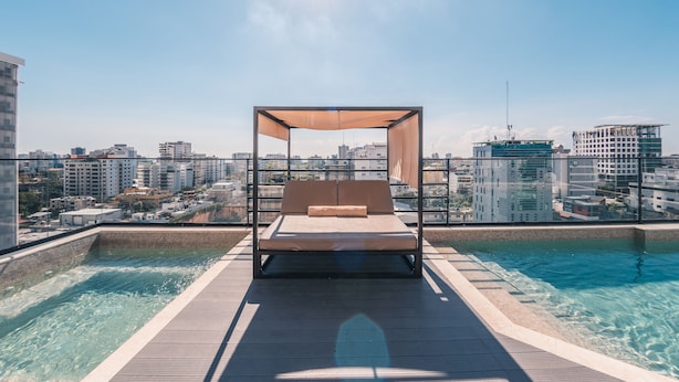 Un espace piscine aménagé sur le toit, avec un lit et un auvent, offrant une vue sur le paysage urbain.