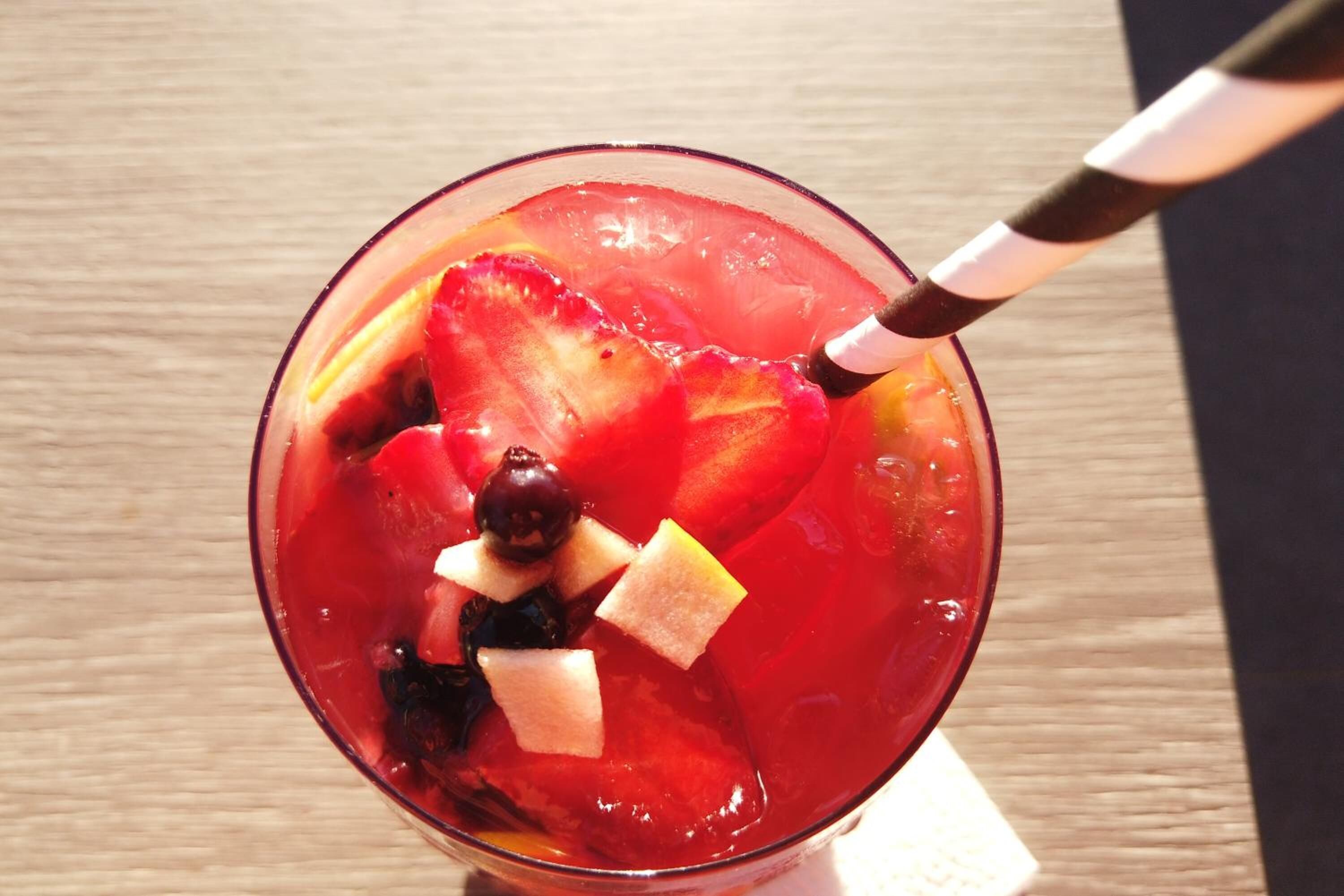 A glass with a red beverage, ice cubes, and fruit pieces.