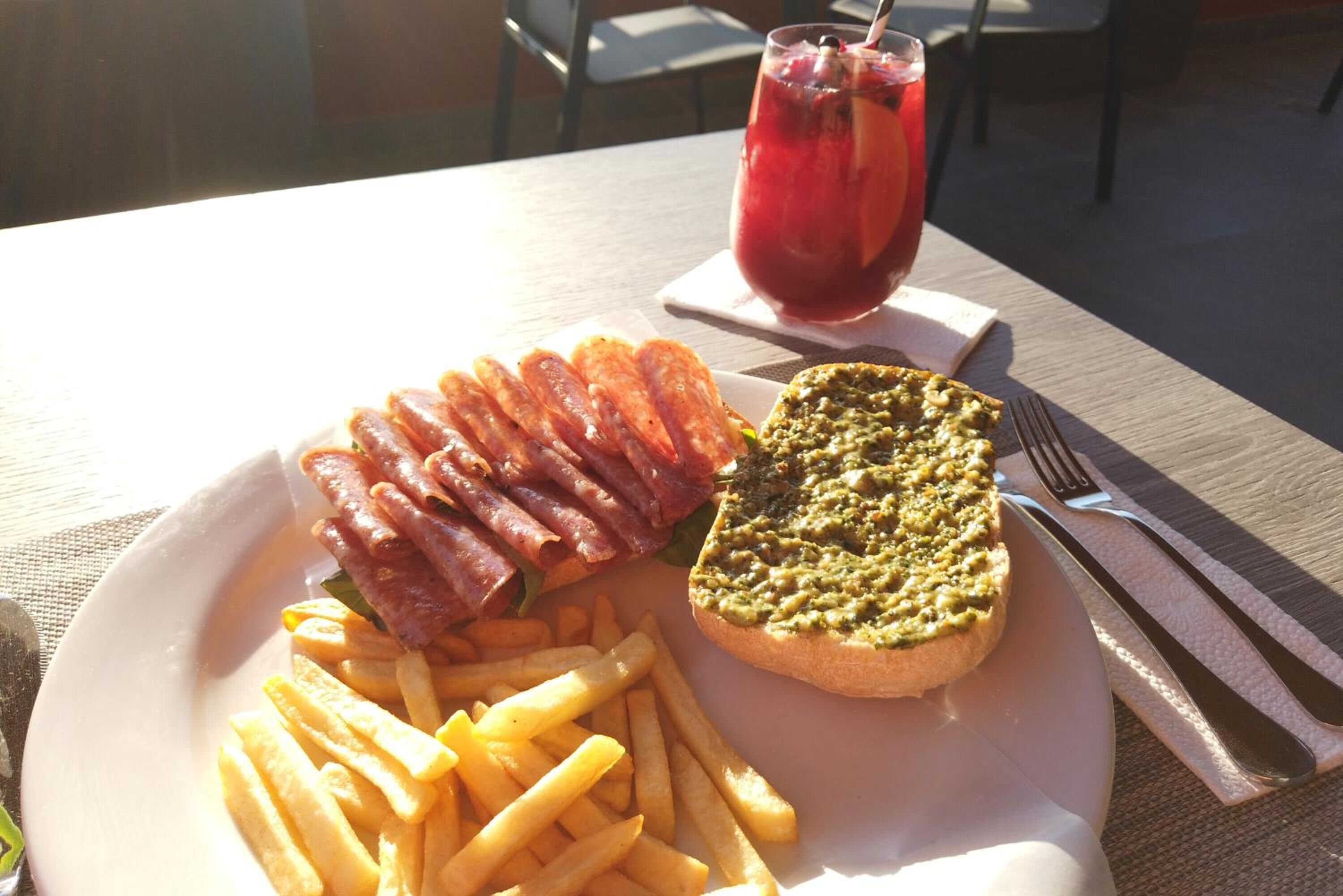 A plate with bacon, fries, and a sandwich on a table with a drink and cutlery.