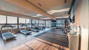 Une salle de sport spacieuse équipée de tapis de course, de vélos elliptiques et d’un distributeur d’eau.