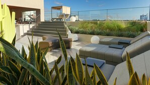 Un salon sur le toit, doté d’un espace extérieur aménagé, d’un escalier et offrant une vue sur le panorama urbain.
