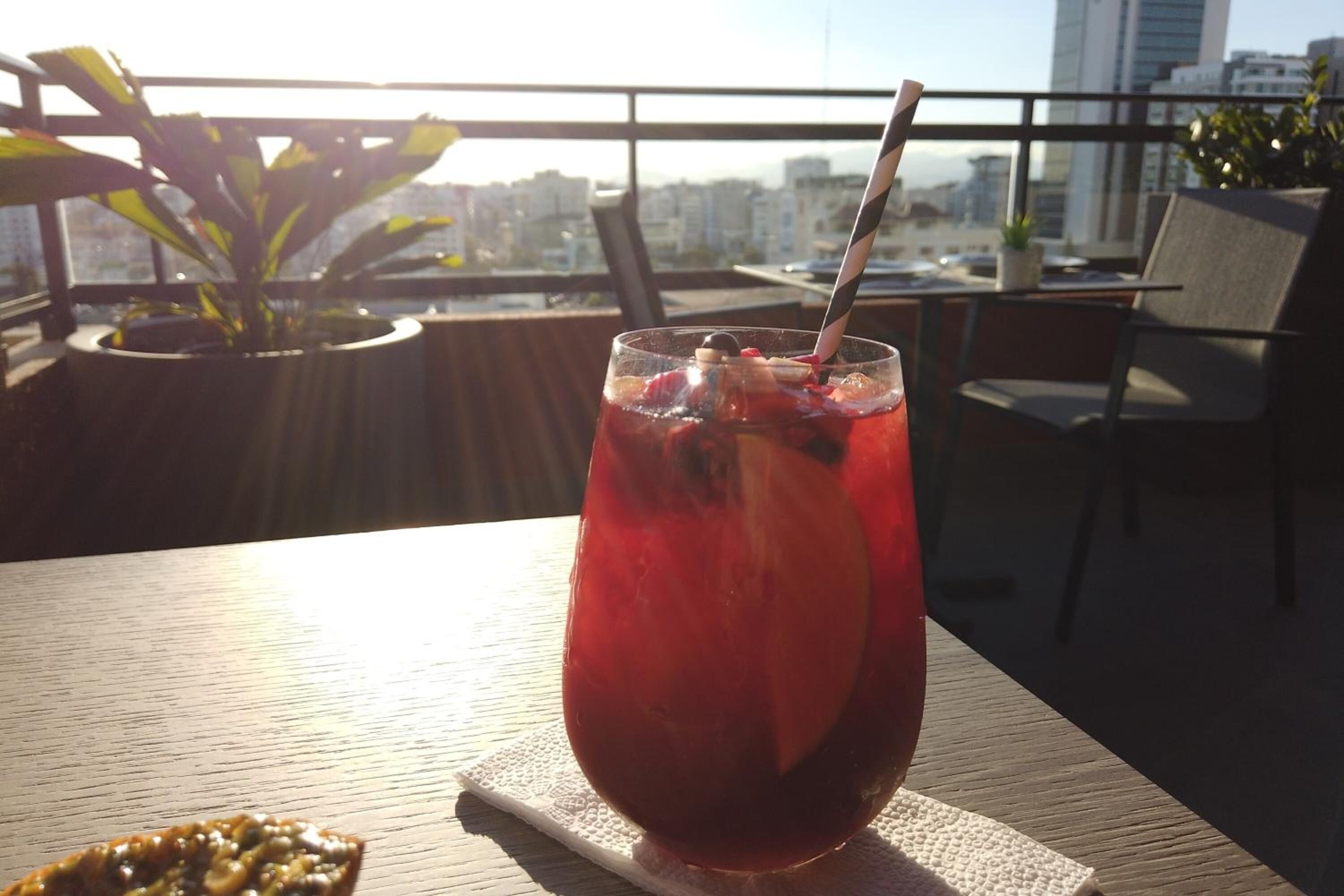 A glass of red beverage on a table with a city view in the background.