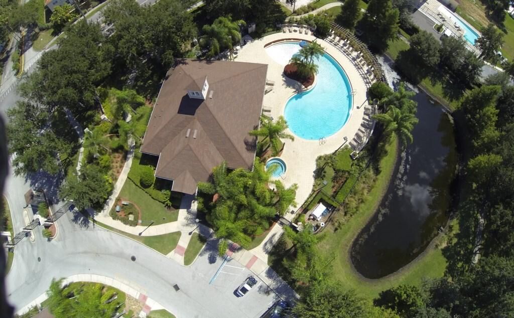 An aerial view of a property with a swimming pool, a covered patio, and a large house with a sloped roof.