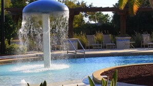 A swimming pool with a central water feature, surrounded by lounge chairs and a pergola.