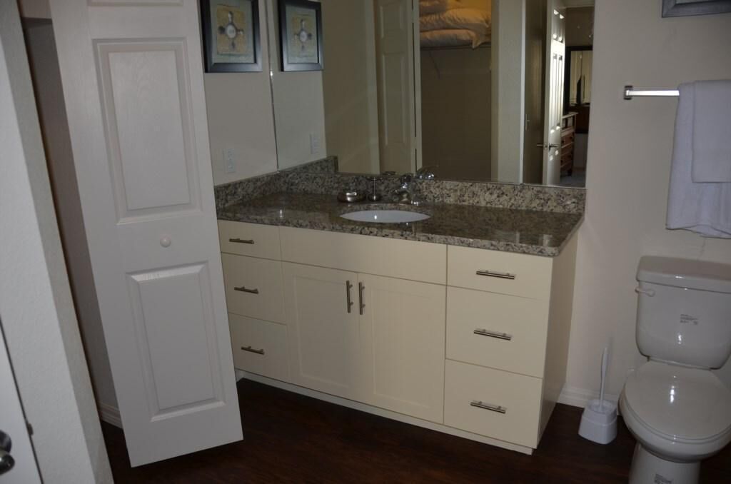 A bathroom with a white toilet, a sink with a granite countertop, and a mirror above the sink.