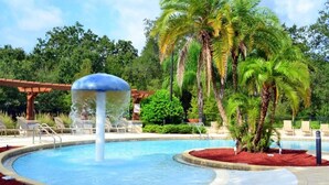 A pool with a water feature, surrounded by palm trees and lounge chairs.