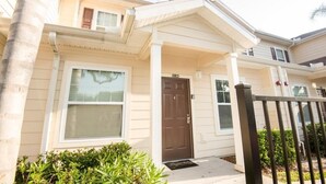A two-story residential building with a front porch, a brown door, and a mailbox.