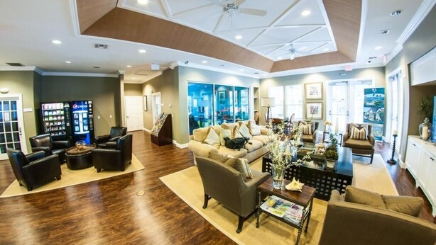 A spacious living area with a high ceiling, a central seating arrangement, and a view of the city through large windows.
