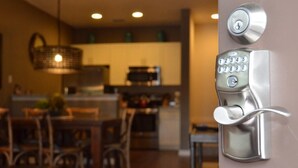 Una cocina moderna con microondas y estufa integrados, una zona de comedor con sillas de madera y una cerradura electrónica de teclado en la pared.