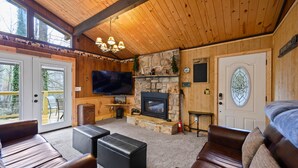 A cozy living room with a stone fireplace, leather couches, a flat-screen TV, and a wooden ceiling.