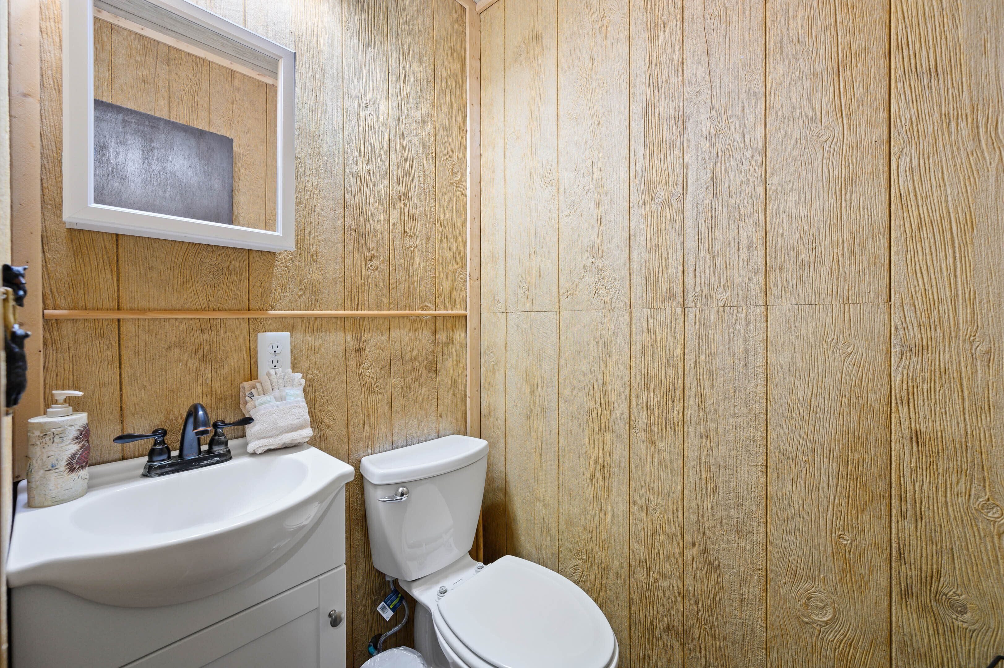 A bathroom with a wooden wall, a white sink, a toilet, and a mirror above the sink.