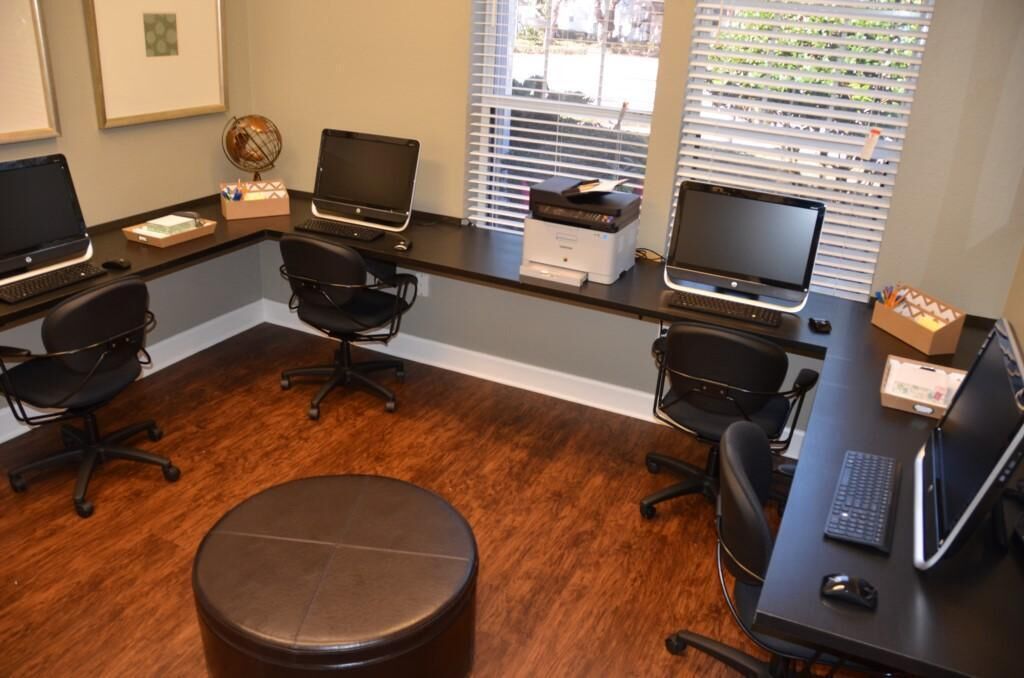 A professional office with three desks, each with a computer and chair, and a central round table.
