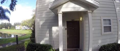 Una casa de un piso con puerta principal marrón oscuro, revestimiento blanco y un pequeño porche.