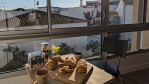 A breakfast setup with croissants, coffee, and a box of Saint Louis Les Bouchies on a wooden table by a window. - Sol-y-Days Murènes 1, large studio close to beaches and center (Le Grau-du-Roi)
