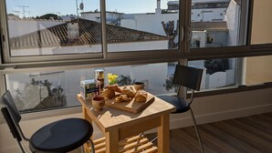 A dining area with a table set for breakfast, including croissants and coffee, and a view of the city through large windows. - Sol-y-Days Murènes 1, large studio close to beaches and center (Le Grau-du-Roi)
