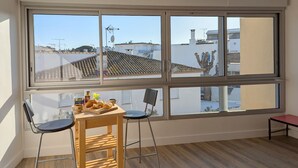 A room with a large window, a wooden table with pastries, two chairs, and a small stool. - Sol-y-Days Murènes 1, large studio close to beaches and center (Le Grau-du-Roi)