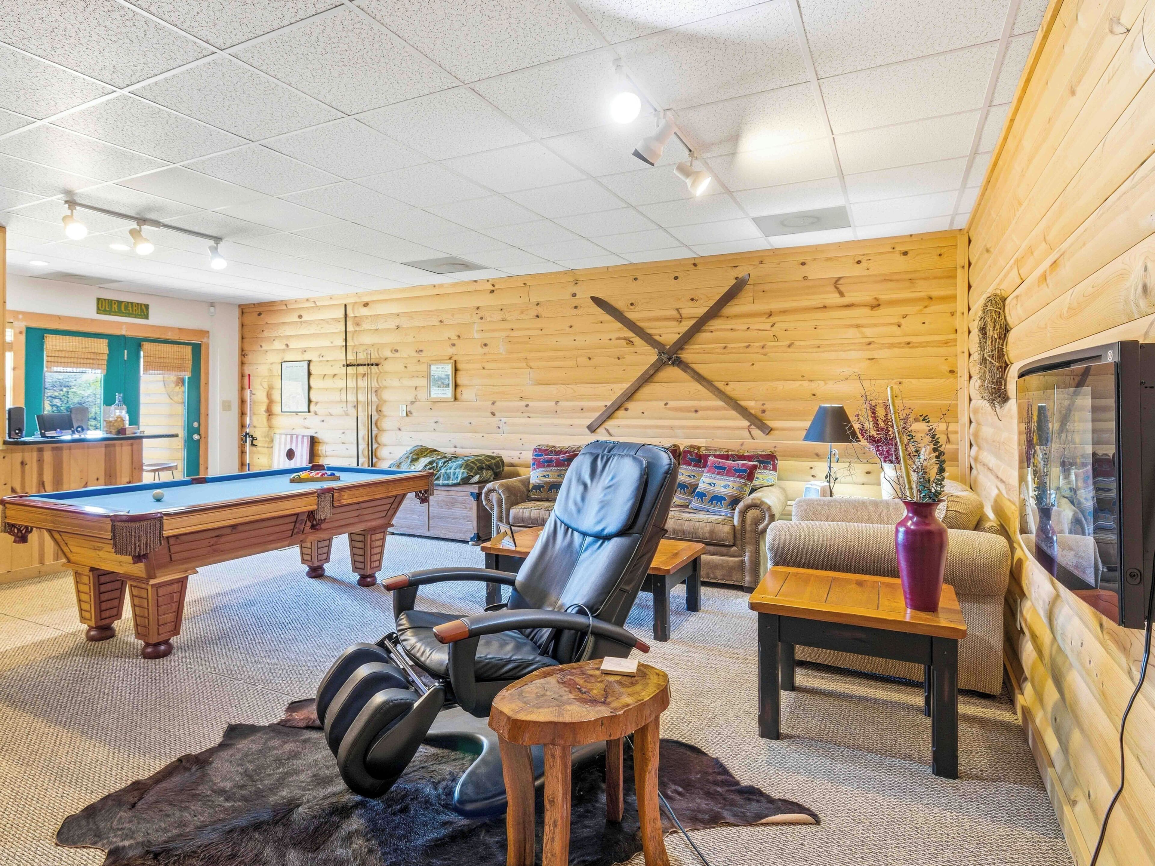 A cozy cabin interior with a pool table, leather chair, and a television.