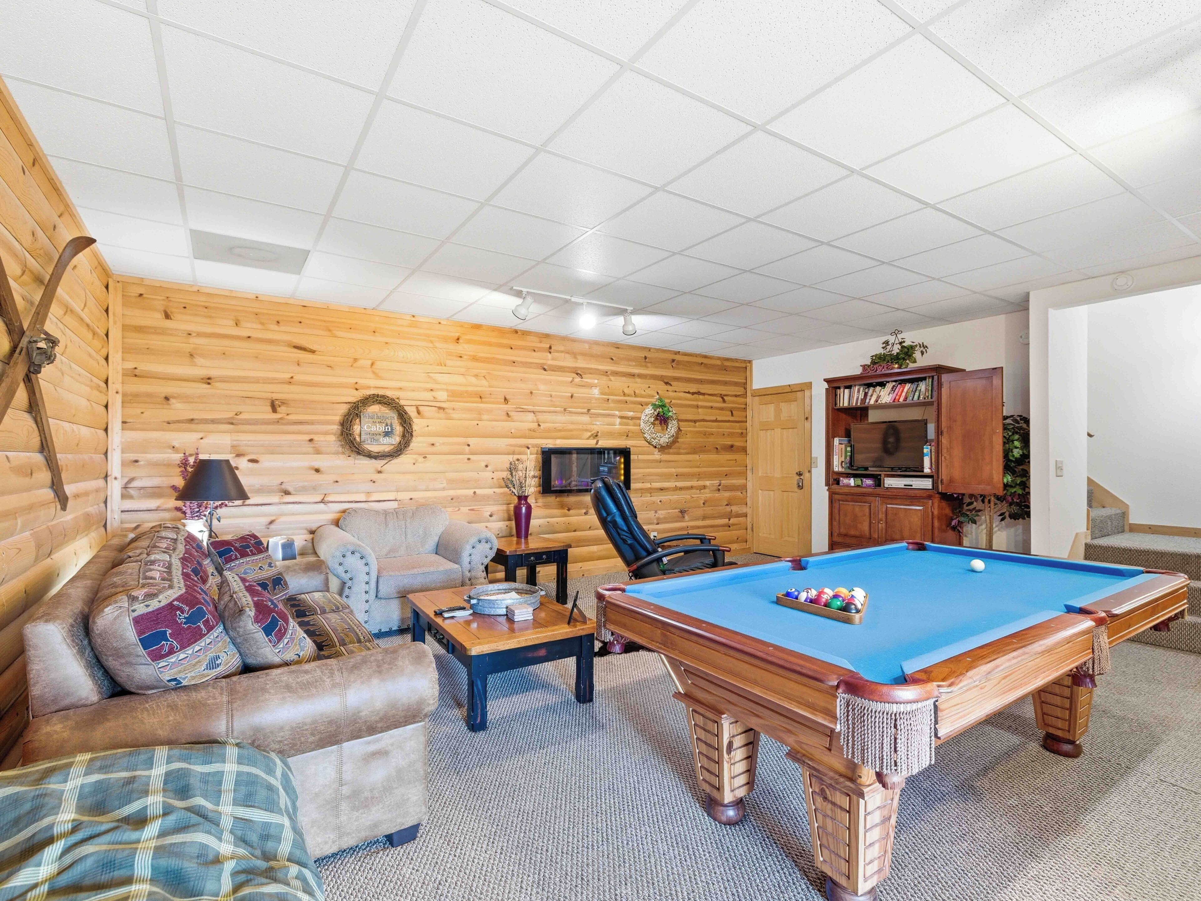 A cozy living room with a pool table, a sofa, and a television.