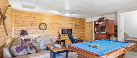 A cozy living room with a pool table, a sofa, and a television.