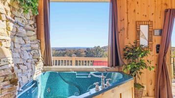 A wooden cabin with a stone wall, a hot tub, and a view of the landscape.