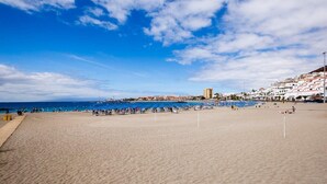 Una playa con cielo despejado, una orilla arenosa y edificios al fondo.