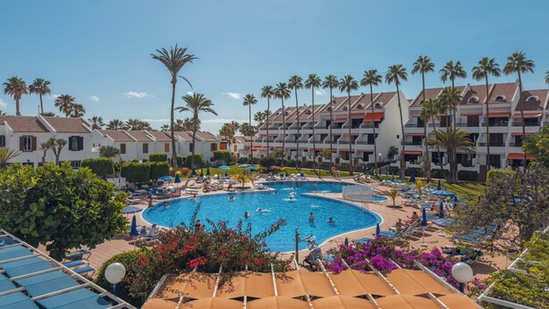 Un hotel con piscina, palmeras y un cielo azul despejado.