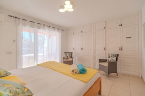 Un dormitorio con cama, dos sillas, un banco y un armario.